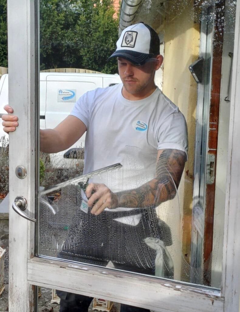 Vinduespudser rengør glasdør med skraber.